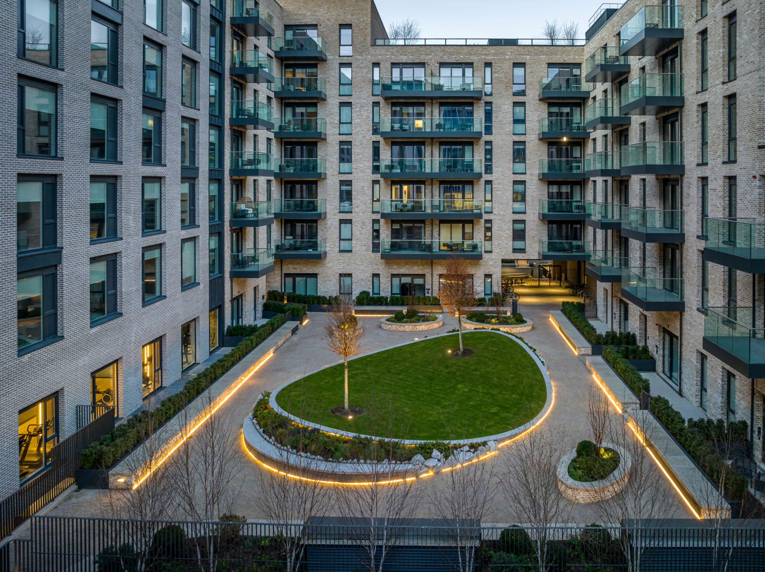 Private landscaped courtyard at Spencer Place Residential, a Ronan Group development in Dublin Docklands, featuring modern apartments, green communal space and premium resident amenities. Large apartments with luxurious terraces surround the lit up courtyard.